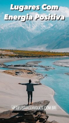 a man standing on top of a rock next to a body of water with mountains in the background