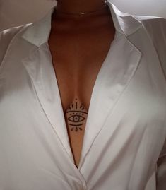 a woman wearing a white shirt with an all seeing eye tattoo on her left chest