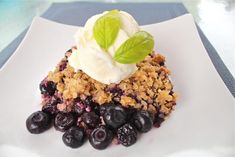 blueberry crumble with ice cream and mint leaves on white square plate, ready to be eaten