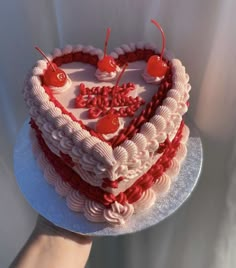 a heart - shaped cake with cherries on top is being held by a person