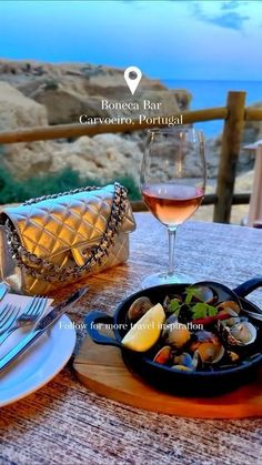 a plate of clams and wine on a table overlooking the ocean