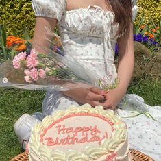 a woman sitting in front of a birthday cake with flowers on the table next to it