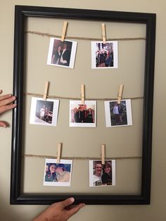 a person holding up a frame with pictures hanging on it and clothes pins attached to the pegs