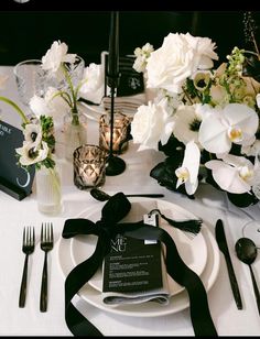 the table is set with white flowers, silverware and black napkins on it