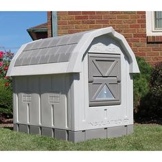 a gray mailbox sitting in the grass next to a brick building with windows on it