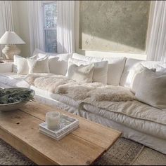 a living room filled with white furniture and pillows on top of a wooden coffee table