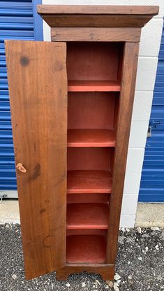 an old wooden bookcase with red paint on the front and bottom shelves, in front of a blue garage door