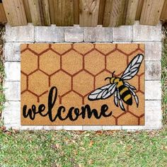 a welcome mat with a bee on it in front of a brick wall and fence