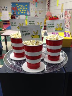 three red and white cups filled with popcorn on top of a plastic tray in a classroom