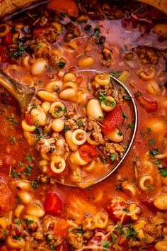 a ladle full of pasta soup with meat and vegetables in it, ready to be eaten