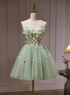 Frolic with grace at your homecoming in this delicately crafted mint green dress that whispers tales of spring! It's a vision of loveliness with its hand-embroidered bodice, where each cherry blossom seems to come alive in a symphony of pinks and greens. The dress boasts a playful sweetheart neckline, inviting admiration and sweet memories. Below the waist, the full skirt blooms like a meadow, with tulle layers that add an air of lightness and joy. Tiny floral accents are sprinkled across the skirt, catching the light and the gaze of onlookers. This dress isn't just a choice for homecoming; it's a promise of a magical evening wrapped in beauty and splendor. Green Short Prom Dress, Dress Green Short, Homecoming Dresses Green, Party Dress Green, Beaded Party Dress, Cute Homecoming Dresses, Green Homecoming Dresses, Floral Prom Dresses, Green Tulle