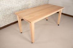 a wooden table sitting on top of a floor next to a white brick wall in an empty room