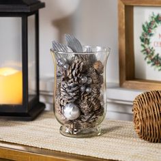 a glass vase filled with pine cones next to a candle and some other items on a table