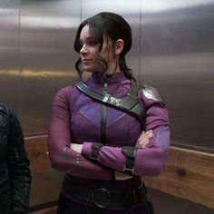 a woman in purple is standing with her arms crossed and looking at the camera while wearing a futuristic outfit