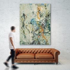 a man walking past a couch in front of a large painting on a white wall