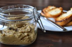 a glass jar filled with food sitting on top of a wooden table next to bread