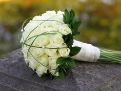 a bouquet of white roses sitting on top of a stone slab with greenery around it