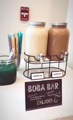 there are three jars on the table with drinks in front of them and a sign that says boba bar