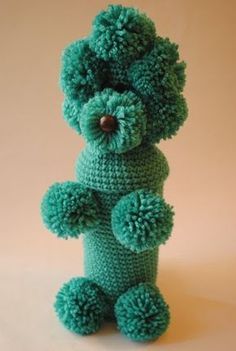 a crocheted green teddy bear with pom - poms