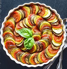 a dish filled with sliced vegetables on top of a black table next to utensils