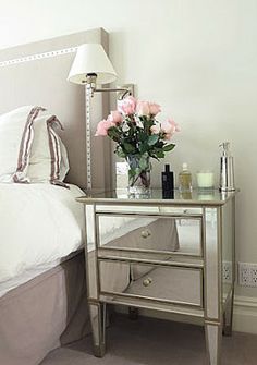 a nightstand with flowers on it next to a bed