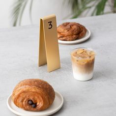 two plates with pastries on them next to a cup of coffee and a table number