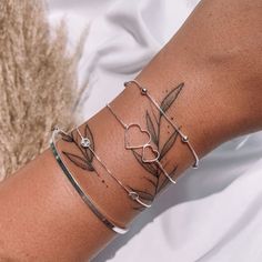 a woman's arm with three bracelets and an arrow tattoo on the wrist