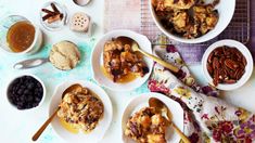 several bowls filled with different types of food on top of a white table cloth next to spoons and utensils