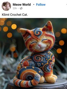 a crocheted cat sitting on top of a wooden stump with lights in the background