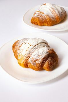 two croissants on white plates with powdered sugar