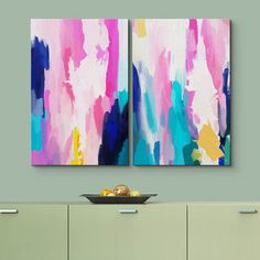 two abstract paintings on the wall above a buffet table with fruit and vases in front of it