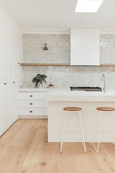 two stools sit in front of an island countertop with white cabinets and tile backsplash