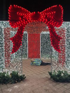 a large red bow on top of a metal pole next to a wall covered in christmas lights