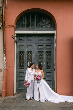 two women standing in front of a door wearing white dresses and holding bouquets with pink flowers