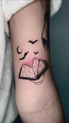 a tattoo on the arm of a woman with an open book and birds flying around