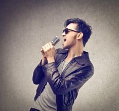 a man singing into a microphone with his hands in the air while wearing sunglasses and a leather jacket