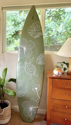 a green surfboard sitting on top of a wooden table next to a lamp and potted plant