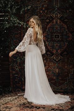 a woman standing in front of a rug wearing a white dress with long sleeves and an open back