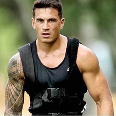 a man with tattoos on his arm and chest is running in a race wearing a black vest