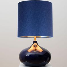 a blue lamp with a gold base on top of a white table and grey background