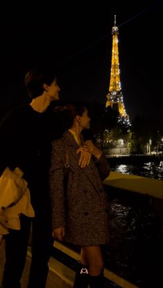 two people standing next to each other in front of the eiffel tower at night