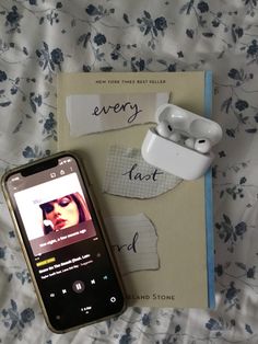 an mp3 player sitting on top of a bed next to a book and earbuds