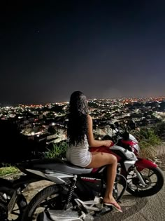 a woman sitting on top of a motorcycle in front of the city lights at night