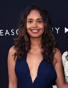 a woman standing in front of a black backdrop wearing a blue dress and smiling at the camera