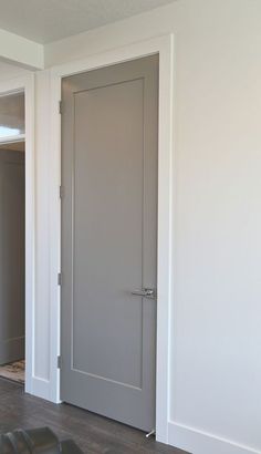 an empty room with white walls and gray door, in the foreground is a black leather chair