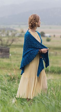 a woman standing in tall grass with a blue shawl over her shoulders and looking off into the distance