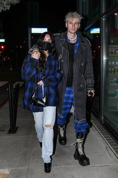 a man and woman are walking down the sidewalk at night with masks on their faces