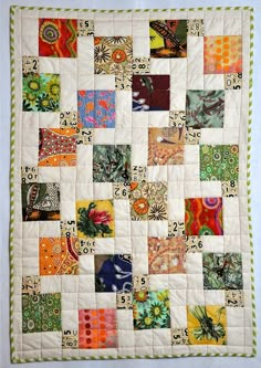 a quilted wall hanging on the side of a white wall with many different colored squares