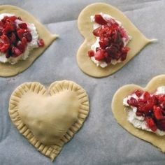 four heart shaped pastries with whipped cream and strawberries on them, sitting on a baking sheet