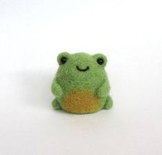 a small green stuffed frog sitting on top of a white surface with its eyes closed